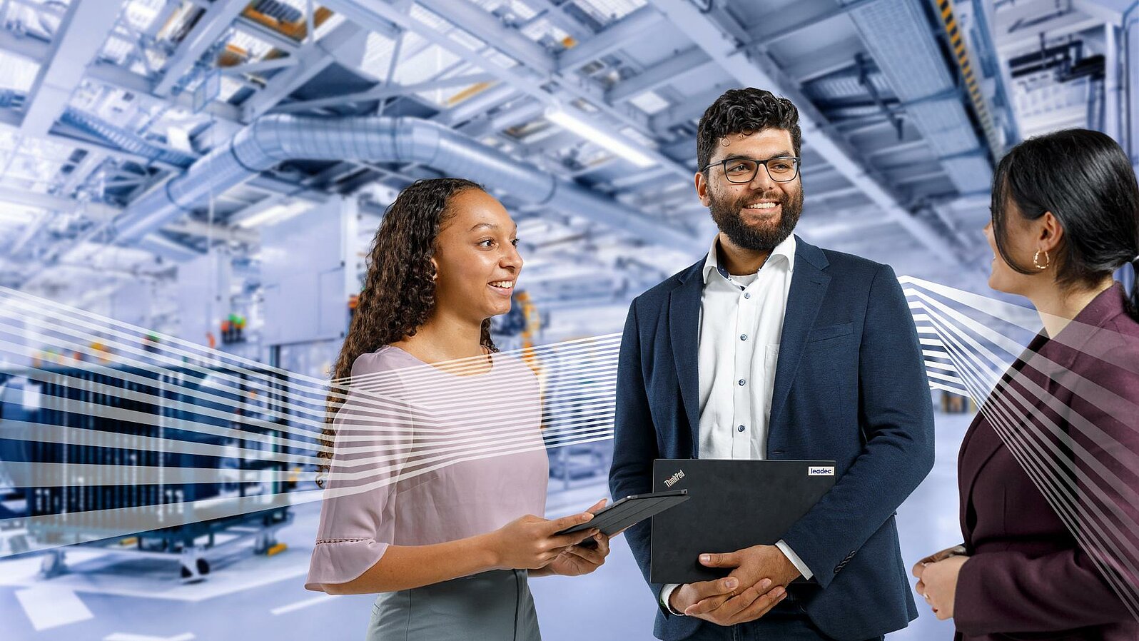 Three Leadec employees in workwear talking in front of a factory background. 